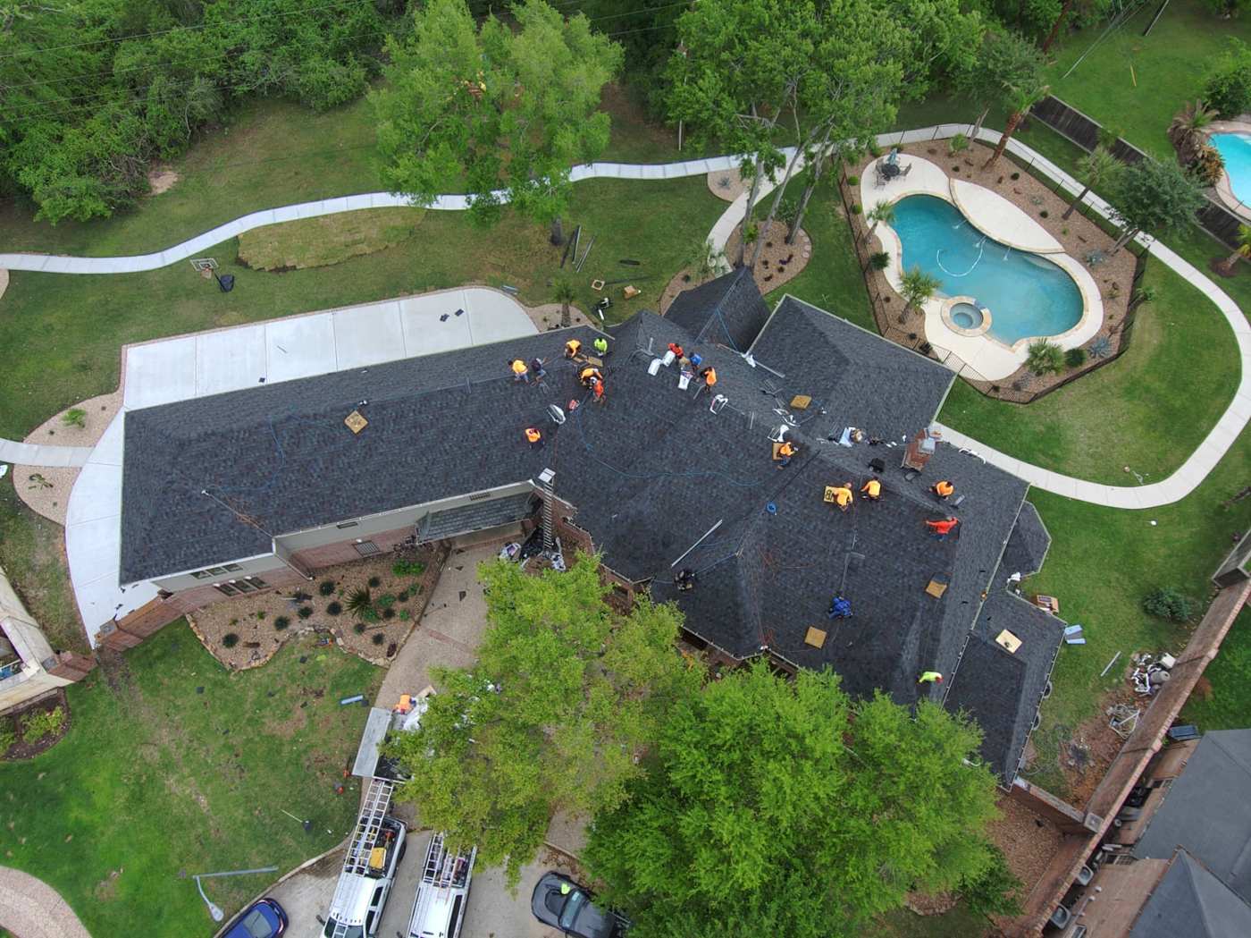Drone photo of a large roofing crew installing shingles on a Houston-area home with a pool