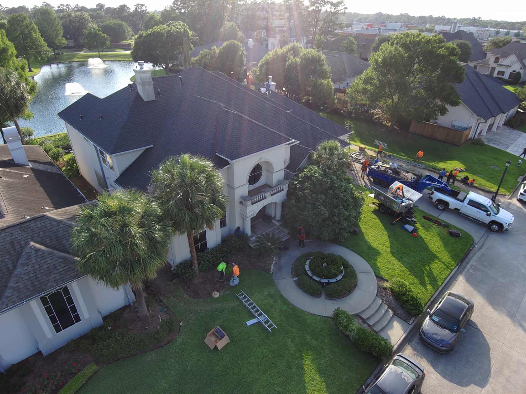 Drone view of a Houston-area lakefront estate with a finished dark shingle roof and the crew loading up at golden hour