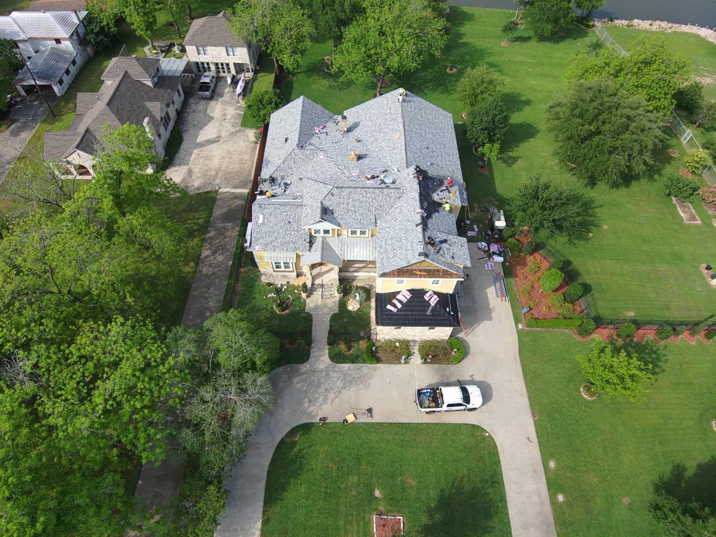 Drone photo of a two-story lake home mid roof replacement with new light gray shingles