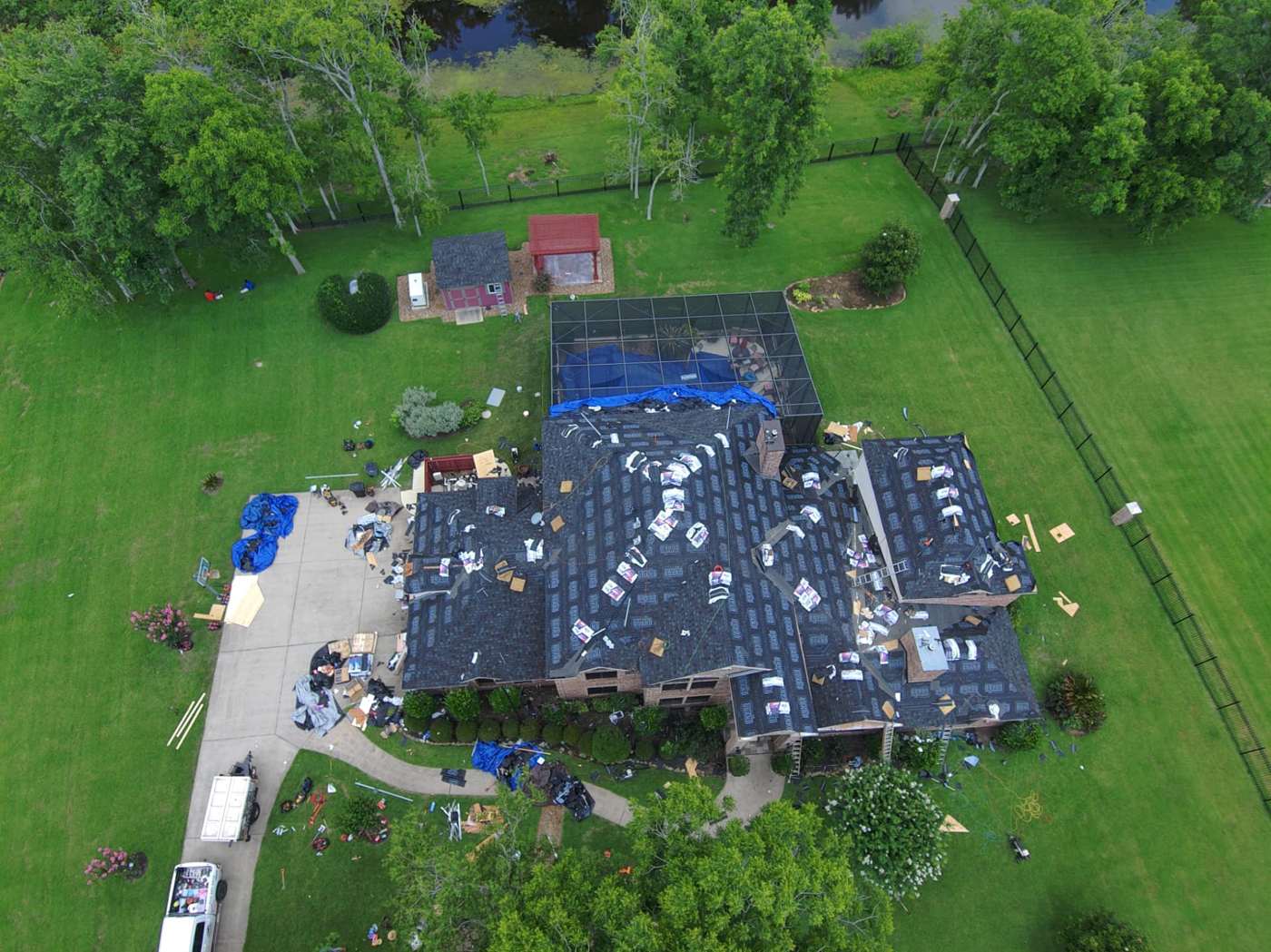 Aerial view of a storm-damaged acreage home tarped and dried in with synthetic underlayment